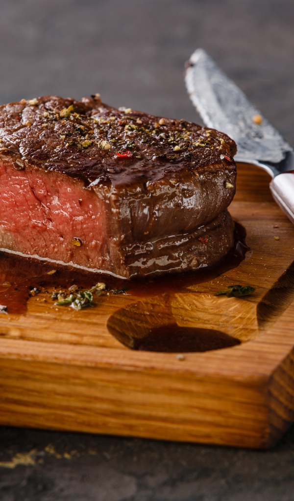 Кусок сочного мяса на доске с ножом и вилкой 