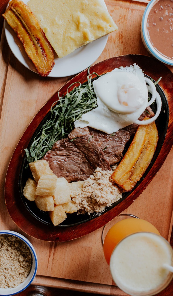 Кусок мяса в жаровне на столе с напитками, овощами и рисом