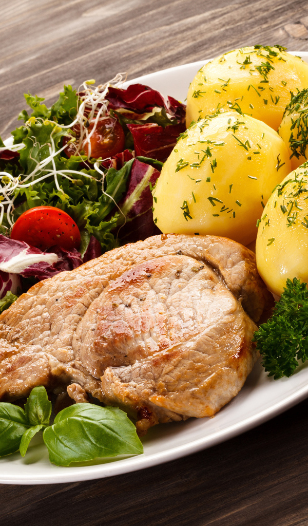 Кусок мяса на тарелке с картофелем и салатом