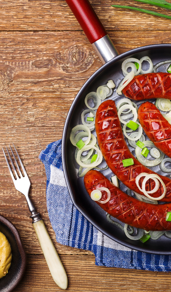 Колбаски барбекю с луком на сковороде на столе с соусом