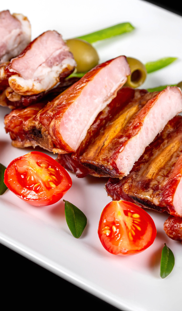 Запеченные ребрышки на белой тарелке с помидорами и оливками