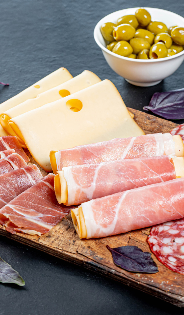 Сыр, бекон и колбаса на разделочной доске на столе с оливками