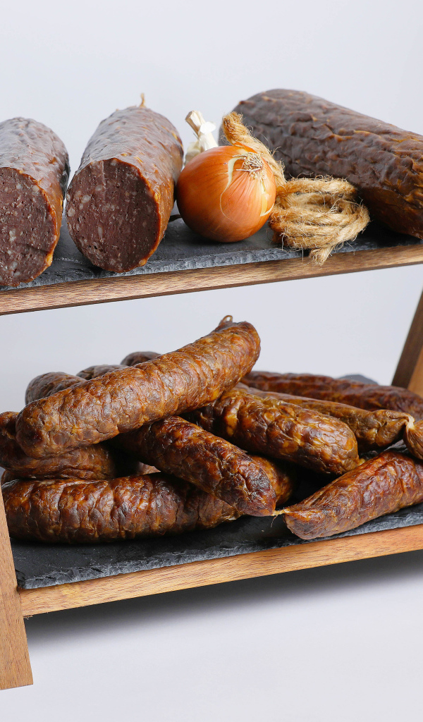 Различные виды колбасы на полке с луком на сером фоне