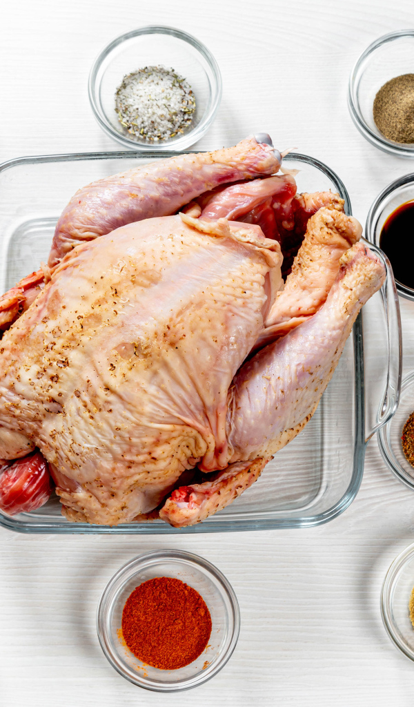 Свежая курица на противне на столе со специями 