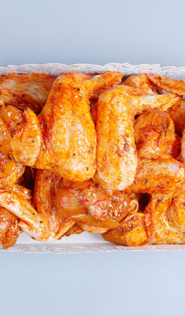 Жареные куриные крылья в белой корзине на сером фоне