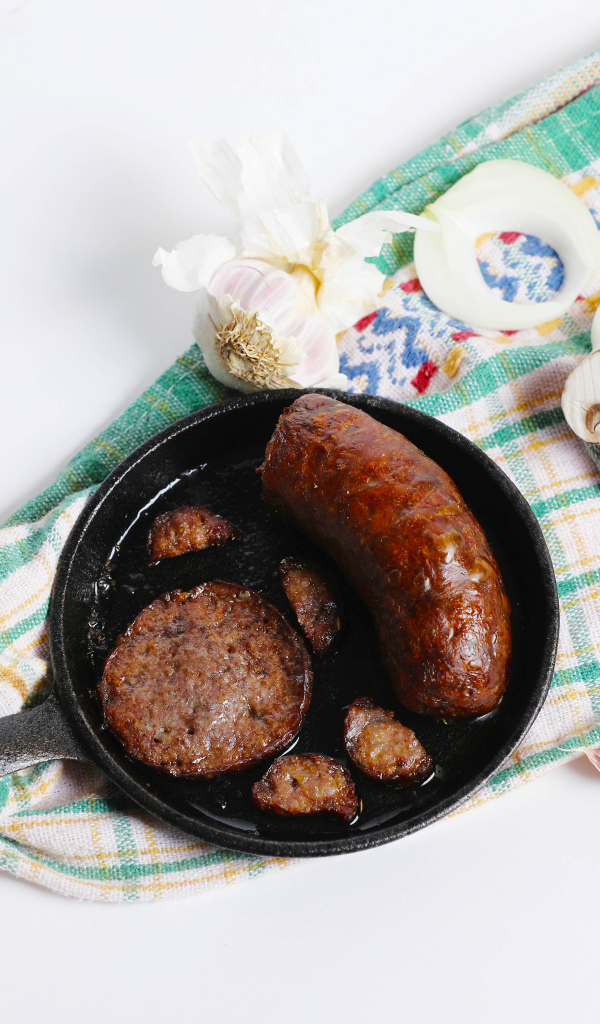 Сковорода с жареной колбасой на столе с полотенцем и чесноком