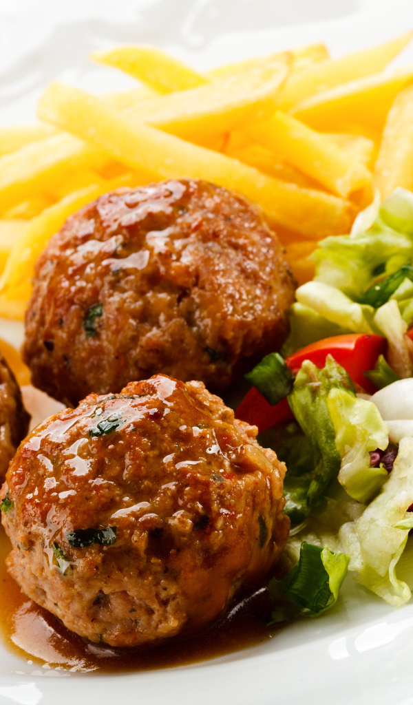 Фрикадельки с салатом и картофелем фри на белой тарелке