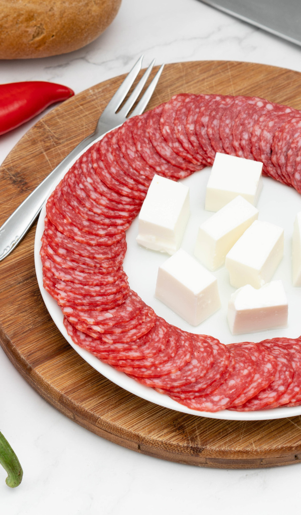 Тарелка с колбасой и сыром на столе с красным перцем