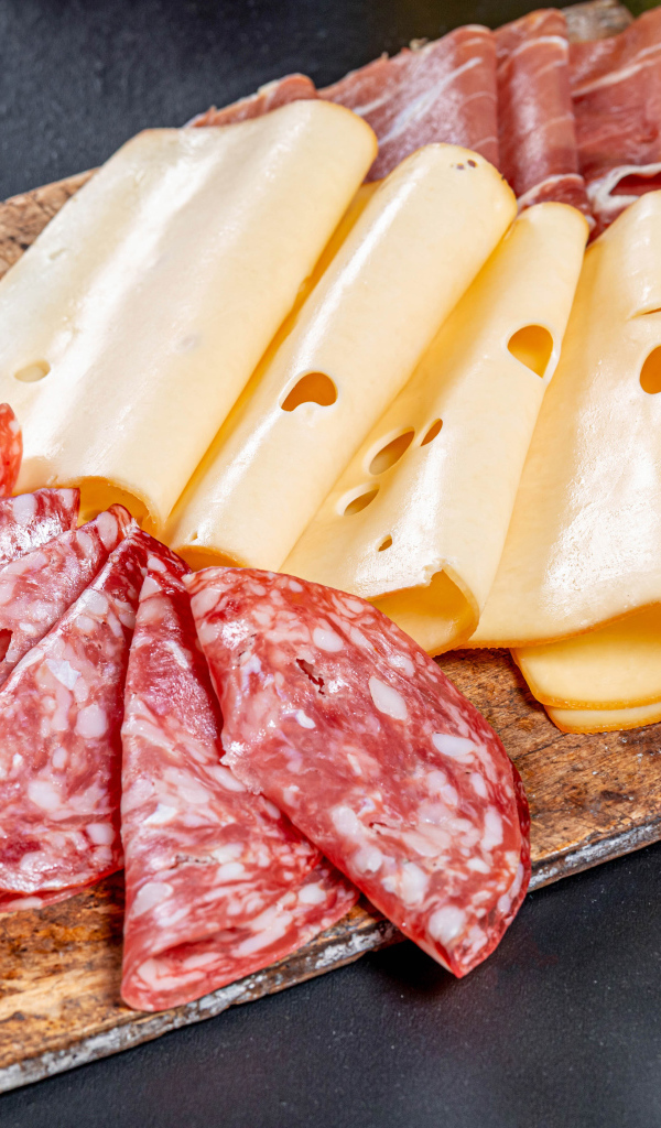 Колбаса, мясо и сыр нарезанный на разделочной доске 