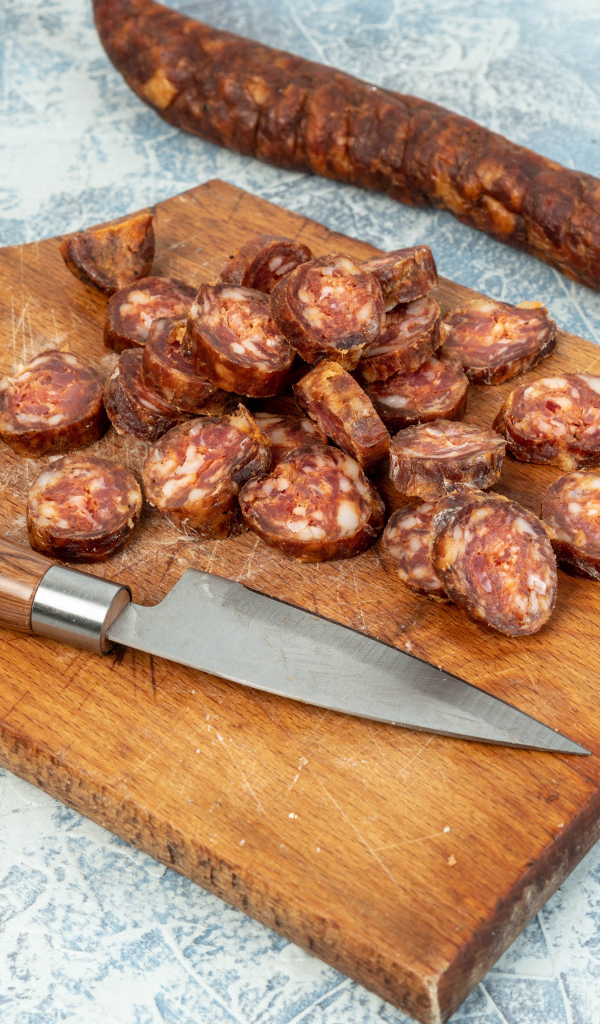 Колбаса нарезана колечками на разделочной доске с ножом 