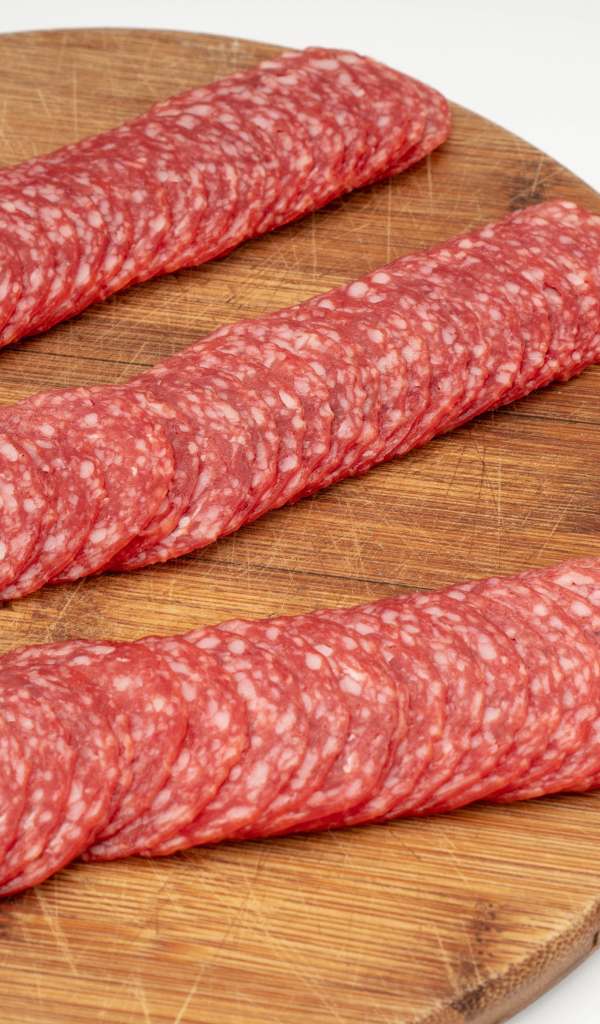 Колбаса тонко нарезана на разделочной доске 