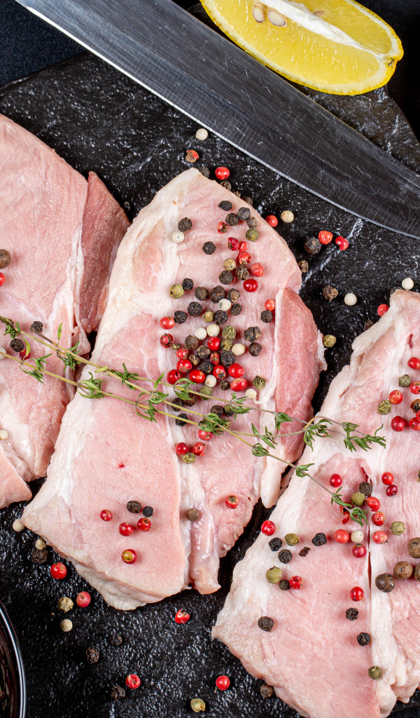 Куски свежего мяса на столе с зернами перца и лимоном