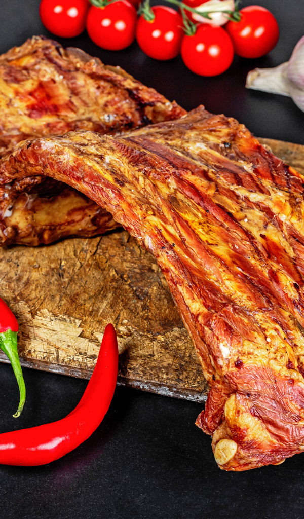 Копченые ребра на столе с красным перцем, чесноком и помидорами