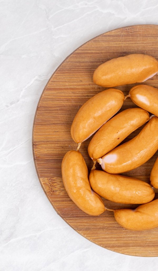 Копченые сардельки на деревянной доске на сером фоне