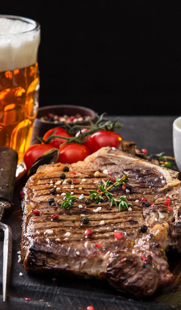 Вкусный кусок мяса на столе с помидорами и бокалом пива