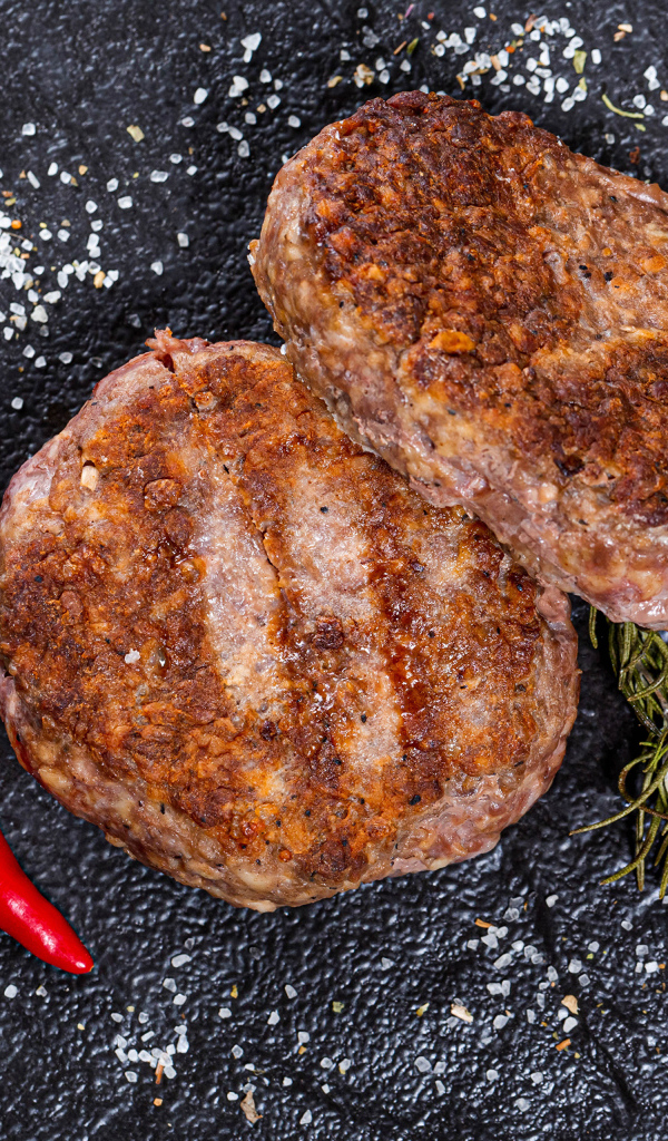 Две котлеты на черной поверхности с красным перцем