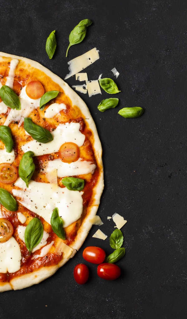 Пицца с сыром, базиликом и помидорами на черном столе 