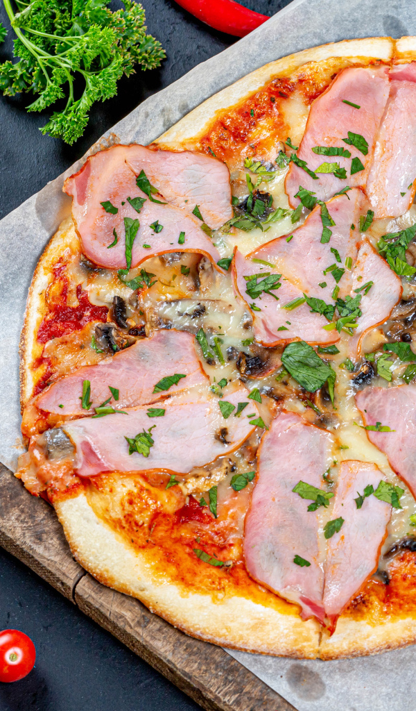 Пицца с ветчиной и грибами на столе с перцем чили, чесноком и петрушкой