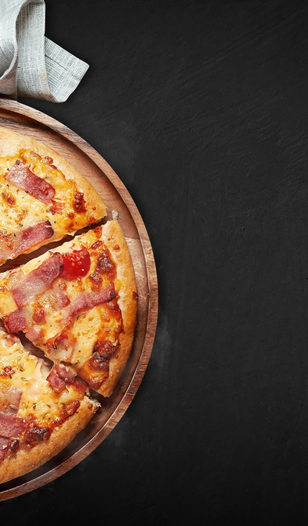 Пицца с кусочками бекона на доске на черном фоне