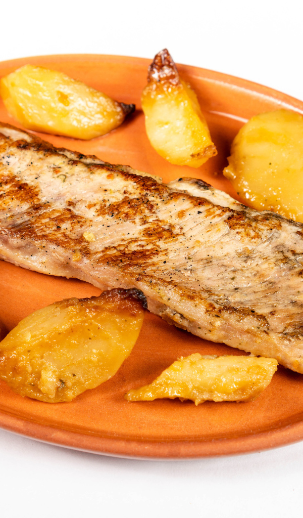 A piece of baked fish on a plate with potatoes