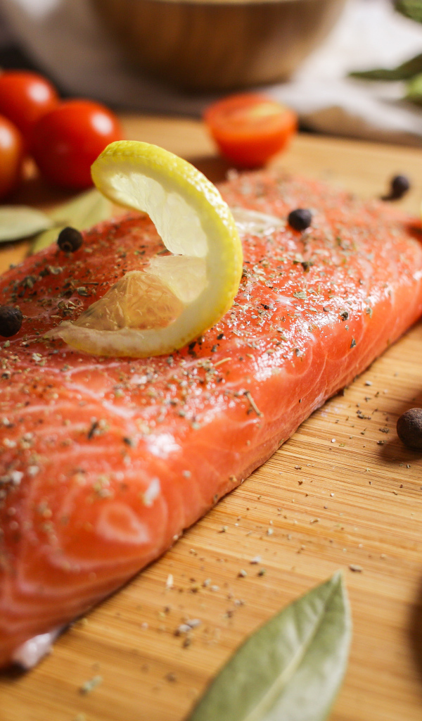 Кусок красной рыбы на доске с лимоном и помидорами