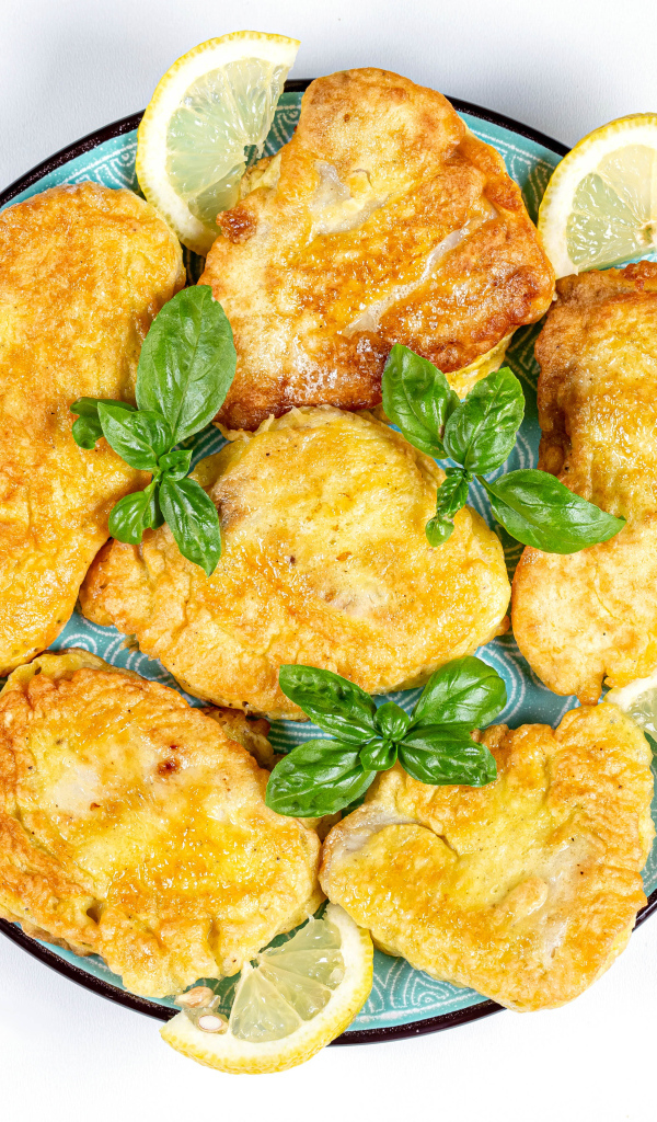 Аппетитная рыба в кляре на тарелке с кусочками лимона и столовыми приборами