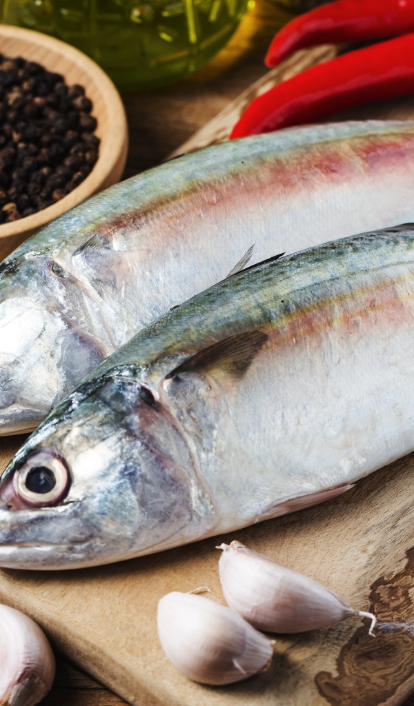 Свежая рыба лежит на доске с чесноком и специями