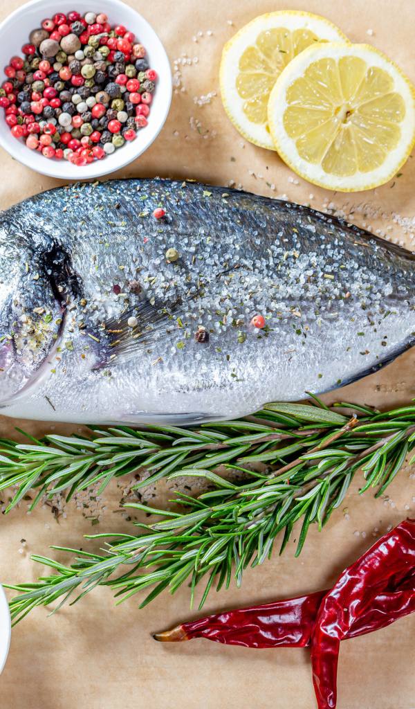 Свежая рыба на столе со специями, лимоном, розмарином и красным перцем