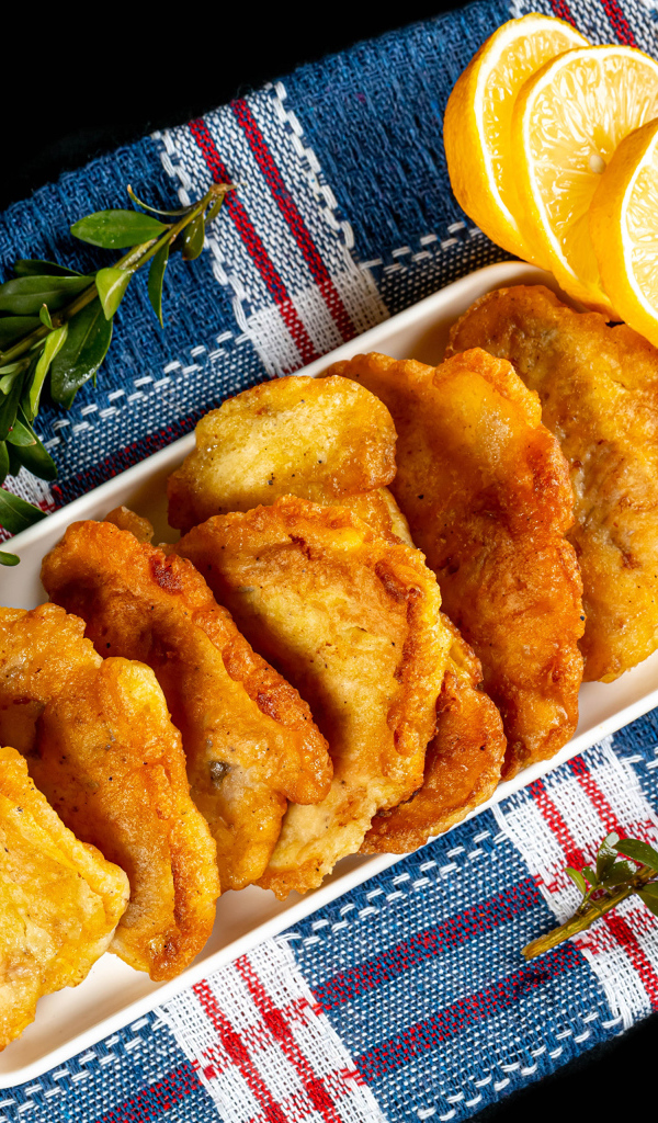 Жареная рыба в кляре на столе с лимоном и зеленью