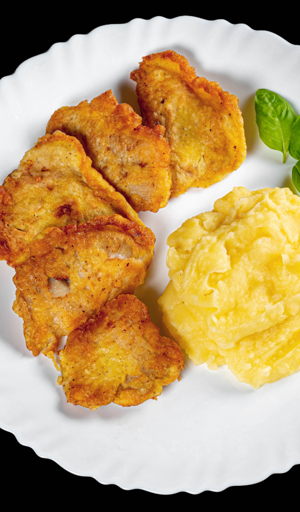 Куски жареной рыбы с картофельным пюре в тарелке на черном фоне