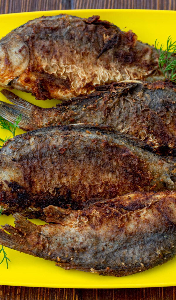 Жареные караси с укропом на желтой тарелке 