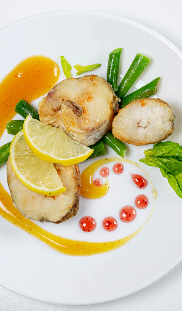 Sliced fried fish on a white plate with lemon and herbs