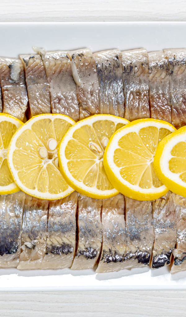 Селедка нарезанная кусочками на белой тарелке с лимоном 