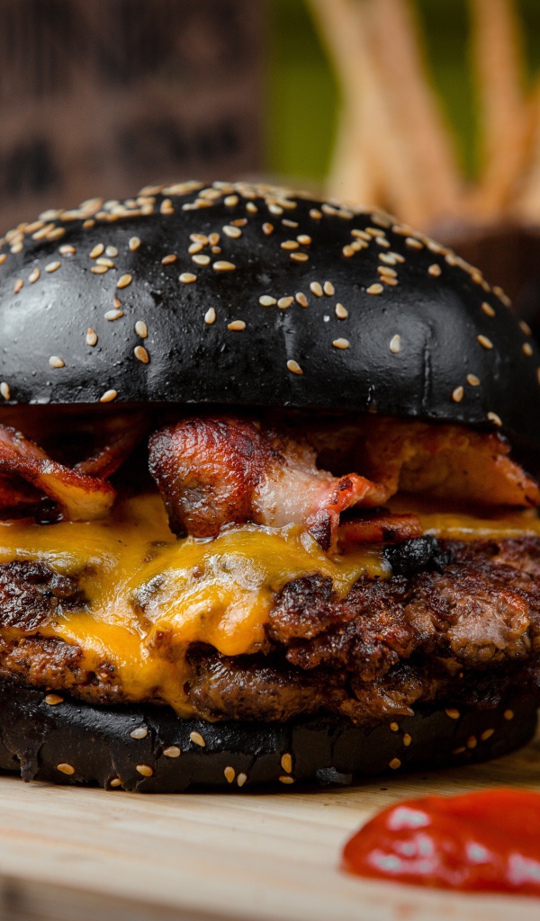 Гамбургер с черной булкой на столе с картофелем фри и красным перцем