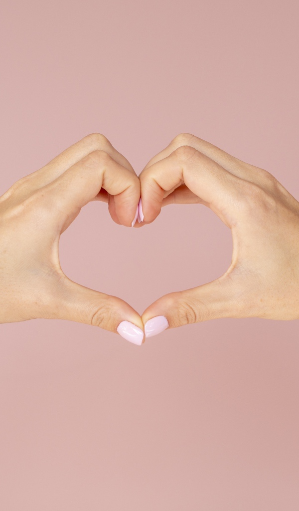 Девушка делает сердце руками на розовом фоне 