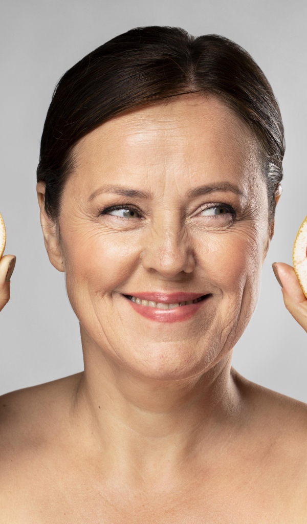 Улыбающаяся женщина с грепфрутом в руках на сером фоне