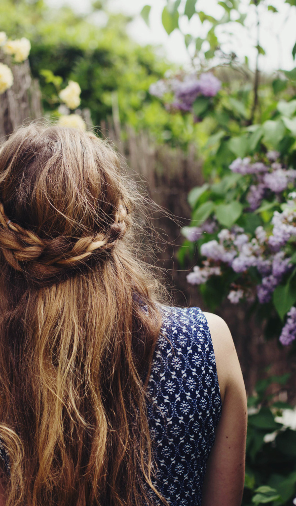 Красивая девушка с косой на голове идет по зарослям сирени 