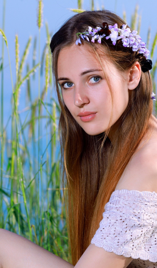 Красивая молодая девушка с венком на голове сидит на поле с колосьями 