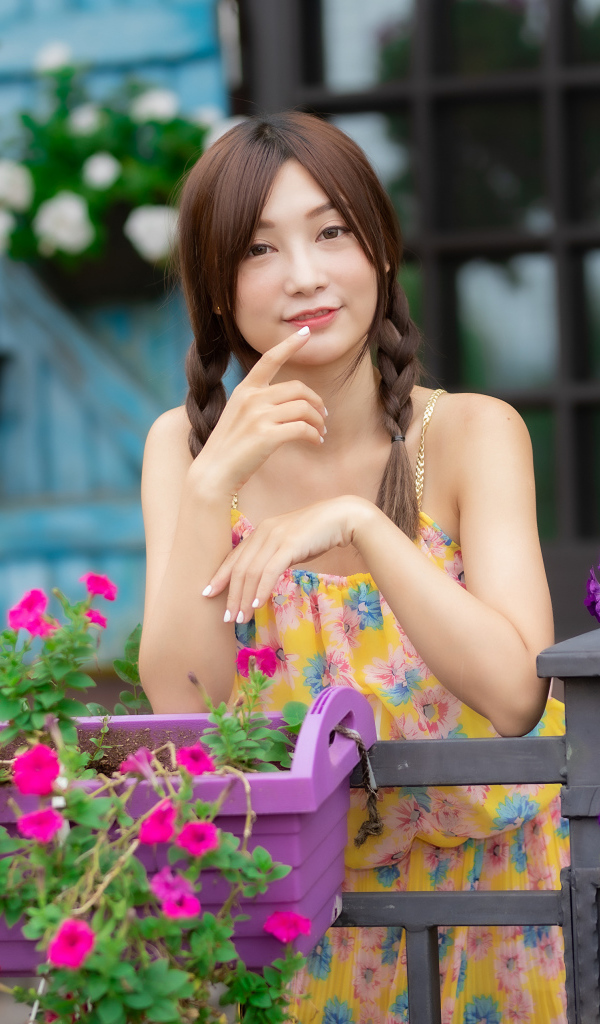 Милая азиатка стоит у кашпо с цветами петунии 