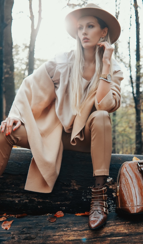 Девушка в пальто сидит на упавшем дереве в лесу 