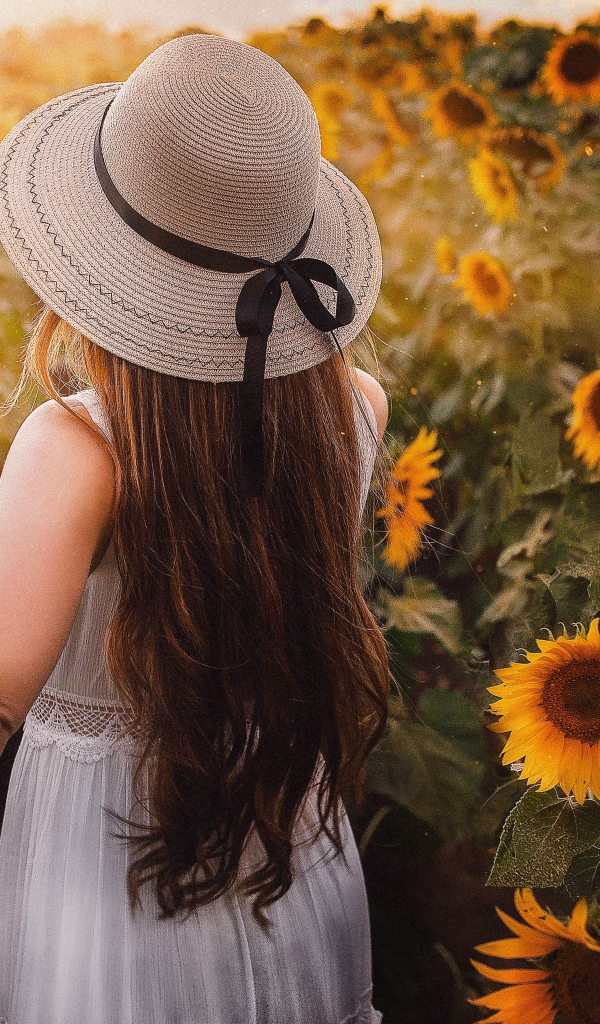 Девушка в белом платье и шляпе гуляет по полю с подсолнухами