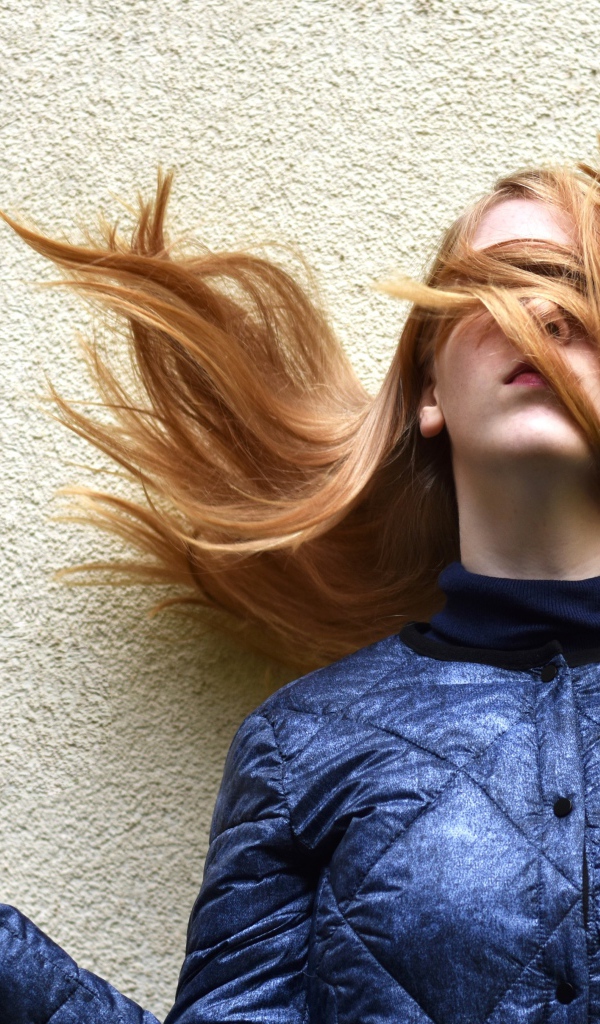 Девушка с волосами на лице стоит у стены