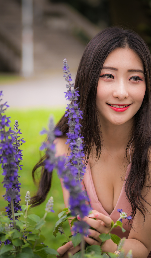 Улыбающаяся азиатка стоит у синих цветов 