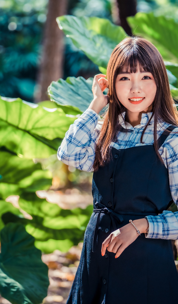 Улыбающаяся девушка азиатка в черном платье стоит в парке