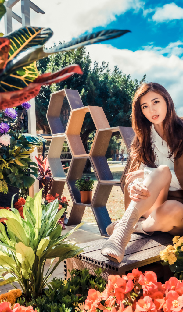 Молодая азиатка сидит возле клумбы с цветами