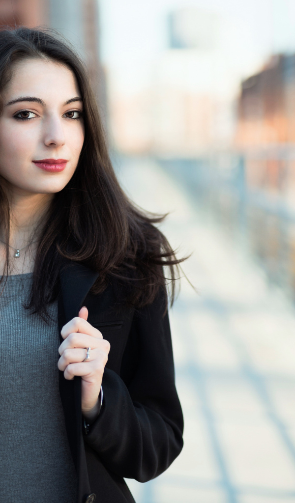 Молодая девушка в черном пальто стоит на мосту