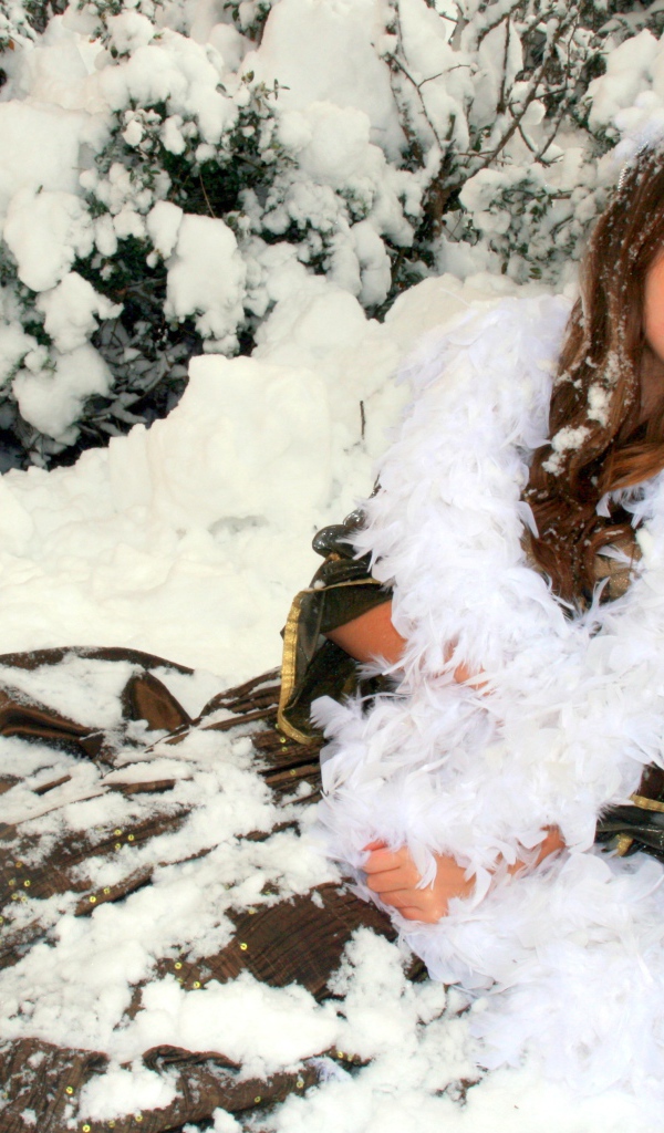 Молодая девушка сидит на снегу под елью 