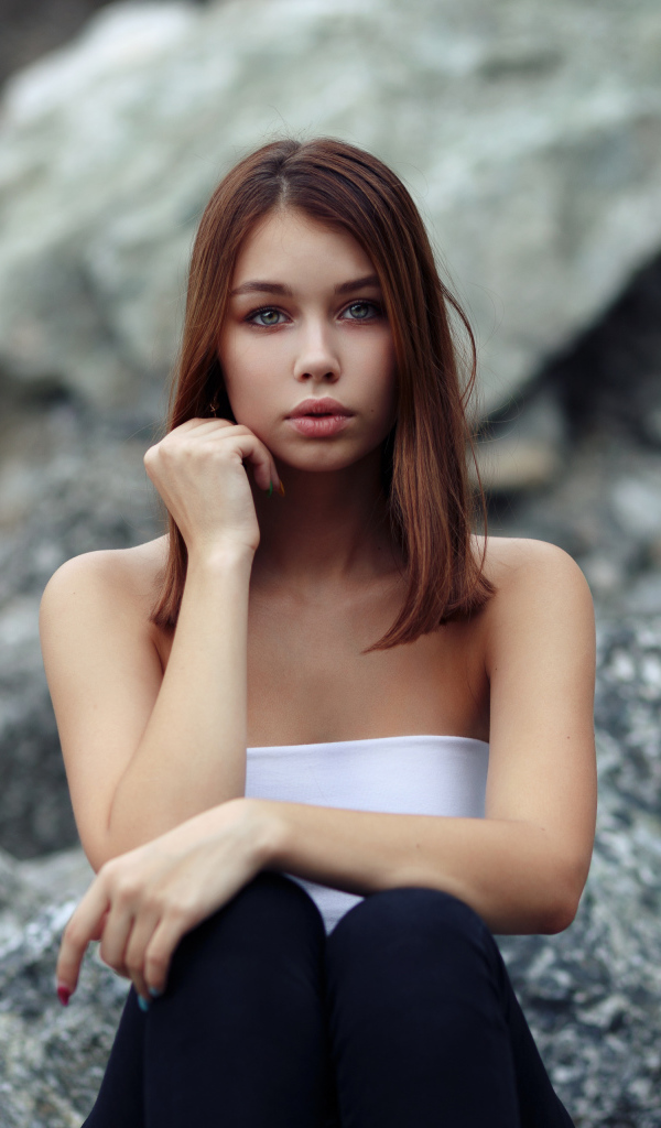 Молодая девушка сидит на камнях 