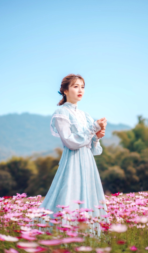 Девушка азиатка в красивом платье идет по полю с цветами космеи