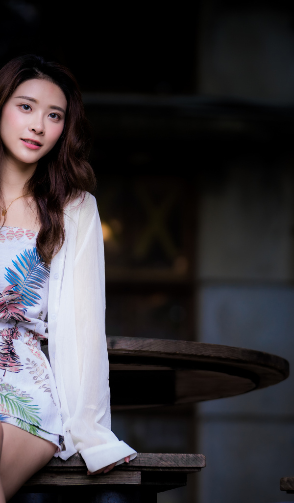 Девушка азиатка в красивом коротком платье сидит на лавке 